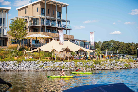 Parque de vacaciones Leukermeer en Limburgo, Países Bajos, con edificios modernos, kayakistas y visitantes junto al agua.