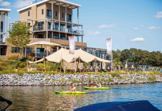 Vakantiepark Leukermeer in Limburg, Netherlands, showing modern lodges, kayakers, and guests relaxing by the water.
