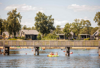 People kayaking and swimming in a lake with holiday homes behind at Vakantiepark Leukermeer, Limburg, Netherlands.