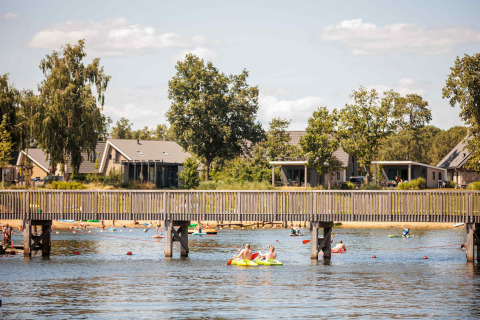 Menschen genießen Wassersport am See mit Ferienhäusern im Hintergrund im Vakantiepark Leukermeer, Limburg.