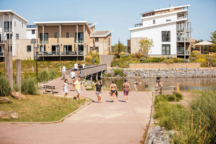 Vakantiepark Leukermeer in Limburgo, Paesi Bassi, con case moderne, lago e persone che passeggiano.