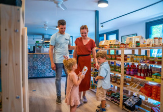 Familie handler sammen i en butik på en feriepark med glamping, omgivet af træhylder med madvarer.