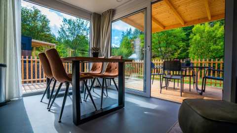 Alojamiento glamping moderno en parque vacacional, comedor interior y terraza amueblada con vista verde.
