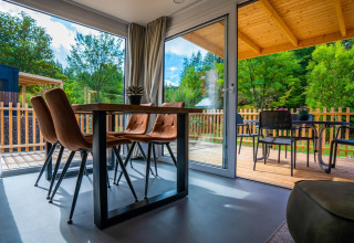 Alojamiento glamping moderno en parque vacacional, comedor interior y terraza amueblada con vista verde.