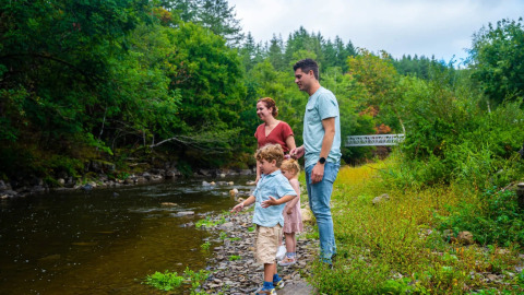 Een gezin geniet bij een rivier in een vakantiepark met glamping, omringd door groene bomen en natuur.