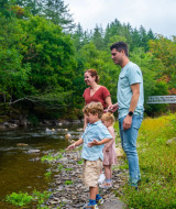 Een gezin geniet bij een rivier in een vakantiepark met glamping, omringd door groene bomen en natuur.