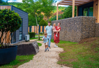 Family walking along a gravel path past modern glamping lodges at a holiday park surrounded by greenery.