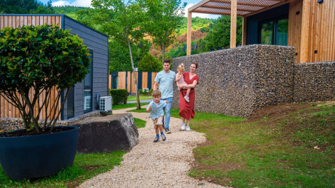 Familia caminando por un sendero de grava junto a modernas cabañas de glamping en un parque de vacaciones verde.
