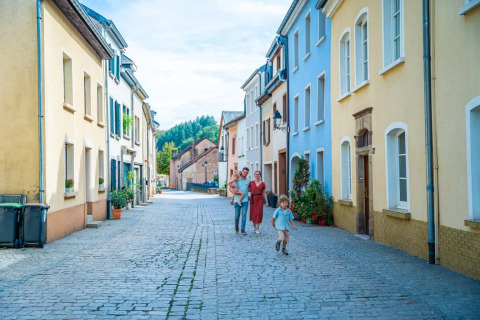 Family walks down a cobblestone street with colorful houses in a peaceful holiday park offering glamping stays.