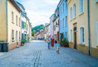 Family walks down a cobblestone street with colorful houses in a peaceful holiday park offering glamping stays.