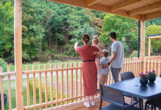 En familie nyder udsigten fra deres glamping-hytte på en feriepark omgivet af grøn skov og natur.