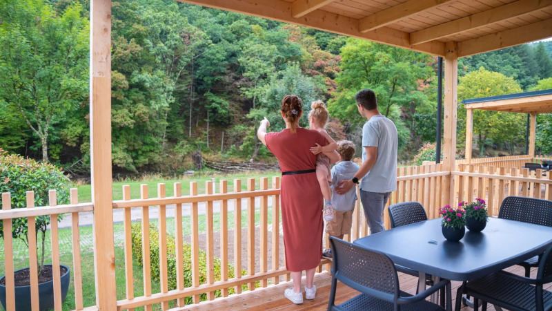 Une famille admire la vue depuis son hébergement glamping dans un parc de vacances entouré de verdure.