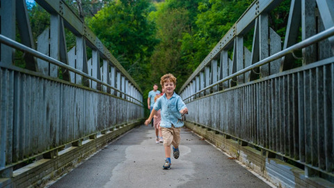 Des enfants courent sur un pont dans un parc de vacances avec hébergements glamping entouré de verdure.