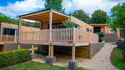 Modern glamping cabins with wooden decks at a holiday park, surrounded by greenery and landscaped paths.