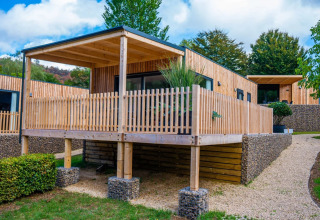 Modern glamping cabins with wooden decks at a holiday park, surrounded by greenery and landscaped paths.