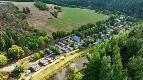 Vista aérea de un parque vacacional con alojamientos glamping, una laguna, árboles y campos verdes.