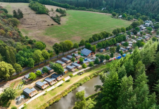 Luftaufnahme eines Ferienparks mit Glamping-Unterkünften, Wald, kleinen Häusern und einem Teich.