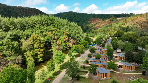 Foto aérea de un parque vacacional con alojamientos glamping, rodeado de bosques y un arroyo natural.