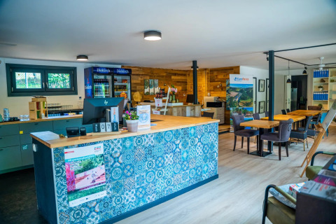 Recepción de parque vacacional con glamping, mostrador colorido, mesas, sillas y neveras de bebidas.