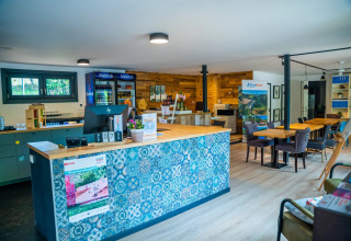 Receptionen i en feriepark med glamping, farverig skranke, borde, stole og køleskabe med drikkevarer.