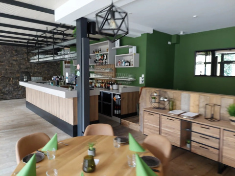 Zona de bar y restaurante moderna con paredes verdes y muebles de madera en un parque de vacaciones glamping.
