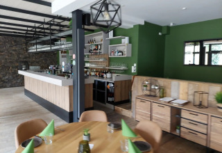 Zona de bar y restaurante moderna con paredes verdes y muebles de madera en un parque de vacaciones glamping.