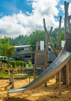 Parque infantil con estructura de madera y tobogán en parque vacacional con glamping, rodeado de árboles.