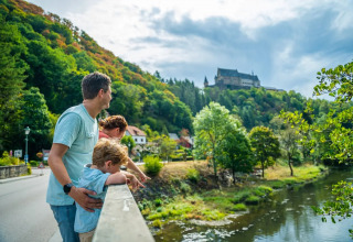 Familia en un puente disfrutando del paisaje de un río, bosque y castillo en un parque vacacional con glamping.