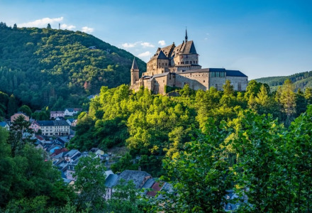 Vista de un castillo en la colina rodeado de bosque y un pueblo pequeño, ideal para glamping vacacional.