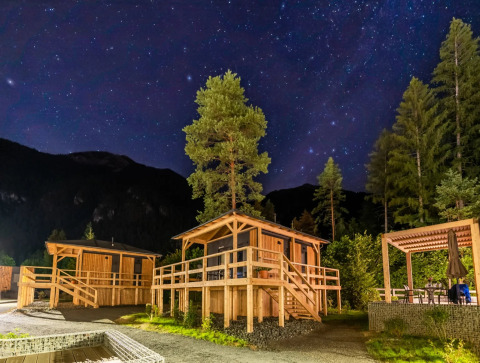 Sterrenhemel boven houten chalets in een vakantiepark tussen de bomen, perfect voor een glampingverblijf.