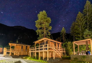 Noche estrellada sobre cabañas de madera en un parque vacacional rodeado de árboles, ideal para glamping.