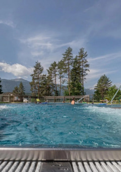 Bubbelend buitenzwembad bij een vakantiepark, omgeven door bomen en bergen op de achtergrond.
