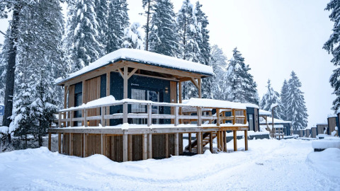 Holzhütte in verschneitem Ferienpark mit Glamping-Angebot. Schnee bedeckt das Dach und die Umgebung.
