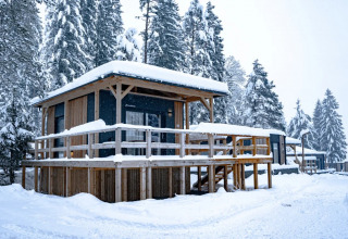 Houten cabine in besneeuwd vakantiepark met glamping accommodaties. Sneeuw ligt op het dak en omgeving.