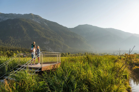 Gezin geniet van uitzicht vanaf platform in vakantiepark met bergen en natuur op de achtergrond.