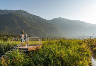 Gezin geniet van uitzicht vanaf platform in vakantiepark met bergen en natuur op de achtergrond.
