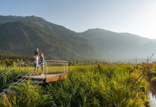 Famille sur une plateforme d'observation dans un parc de vacances entouré de champs et de montagnes.