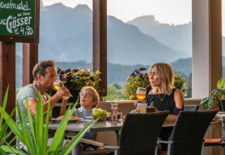 Famiglia che cena e beve su una terrazza di glamping con vista panoramica sulle montagne.