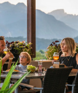 Familia disfruta de cena y bebidas en la terraza de un glamping con vistas a las montañas.