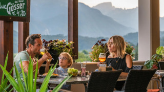 Gezin geniet van diner en drankjes op een glampingterras met uitzicht op de bergen.