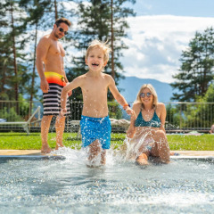 Blije familie geniet bij een zwembad in een vakantiepark met glamping, omgeven door natuur.