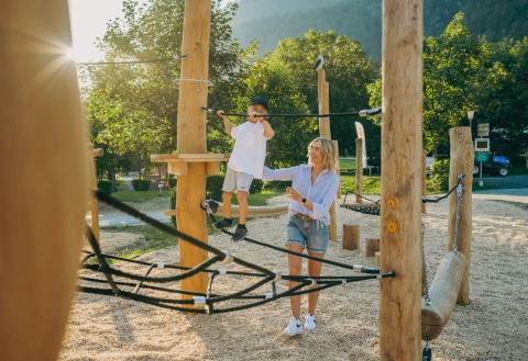 Mamma aiuta il figlio su un percorso avventura in un parco vacanze con sistemazioni glamping.