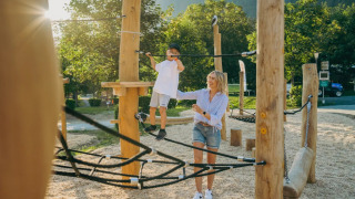 Moeder helpt haar zoon balanceren op het klimparcours in een vakantiepark met glampingaccommodaties.