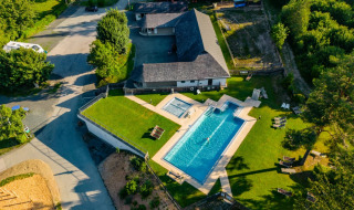 Vista aérea de un parque vacacional con piscina grande, césped verde y zonas de glamping rodeadas de naturaleza.