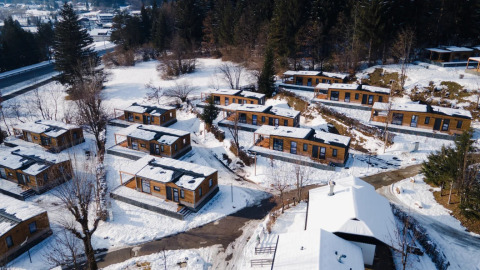 Vista aerea di un villaggio vacanze innevato con cabine glamping tra alberi su una collina in inverno.