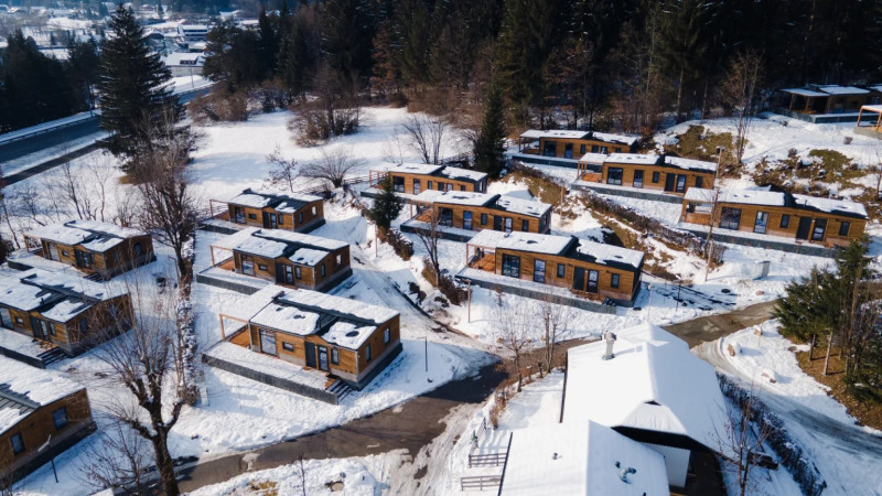 Luchtfoto van een sneeuwrijke vakantiepark met glampinghuisjes, omgeven door bomen op een heuvel.