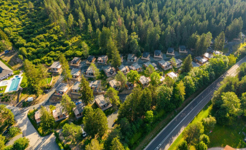 Aerial view of a holiday park featuring glamping cabins nestled in a forest setting near a main road.