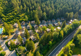 Aerial view of a holiday park featuring glamping cabins nestled in a forest setting near a main road.