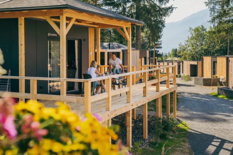 Des vacanciers prennent un repas sur la terrasse d’un lodge glamping dans un parc de vacances au milieu de la nature.