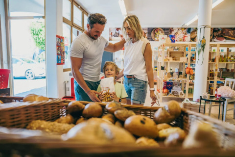 Gezin koopt brood bij de bakker in een vakantiepark met glampingverblijven.